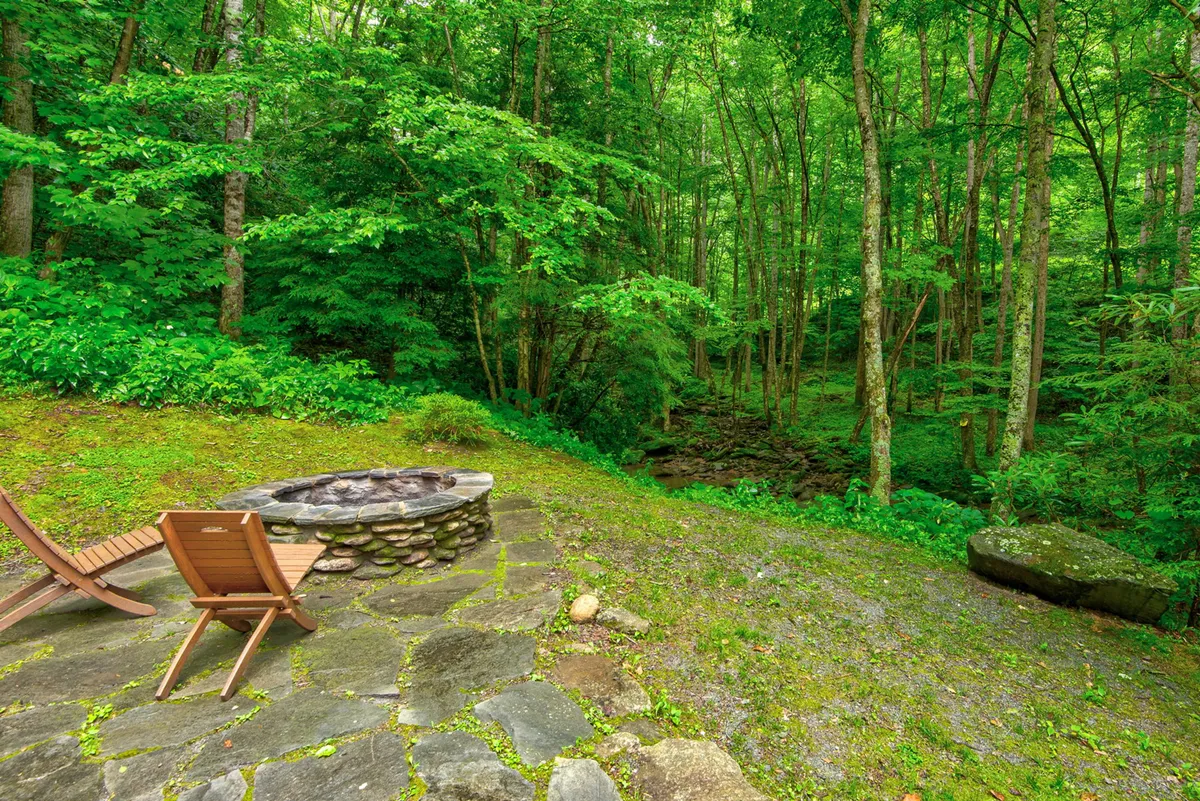A cozy outdoor fire pit area with a wooden chair and dense greenery encircling the scene. The fire pit is ready for gatherings, storytelling, and marshmallow roasting, with sunset lighting adding warmth and tranquility.