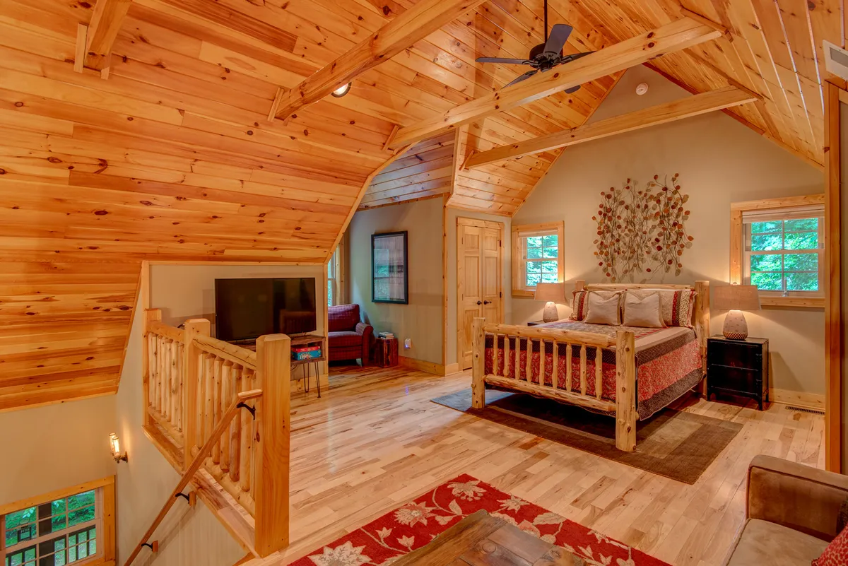 A cozy attic-style bedroom with warm wooden ceilings, a comfortable bed, a sofa area, decorative wall art, and soft lighting. The arrangement creates a welcoming and intimate environment, ideal for families or friends seeking privacy and comfort.