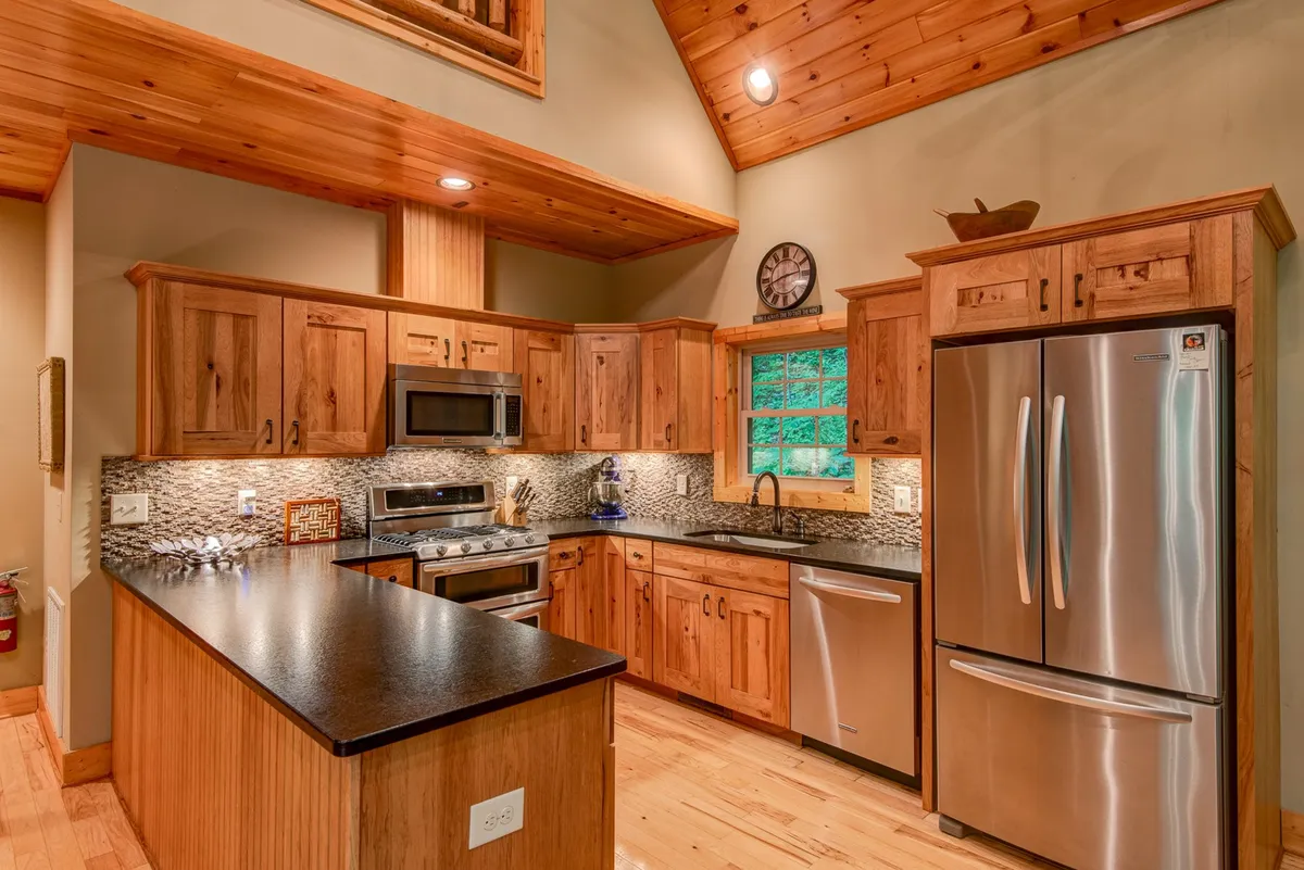 A close-up of the kitchen, featuring custom wood cabinetry, sleek stainless steel appliances including a gas cooktop, and attractive leathered granite countertops. The kitchen window frames inviting greenery from outside, while the layout emphasizes practical space for cooking and gathering.