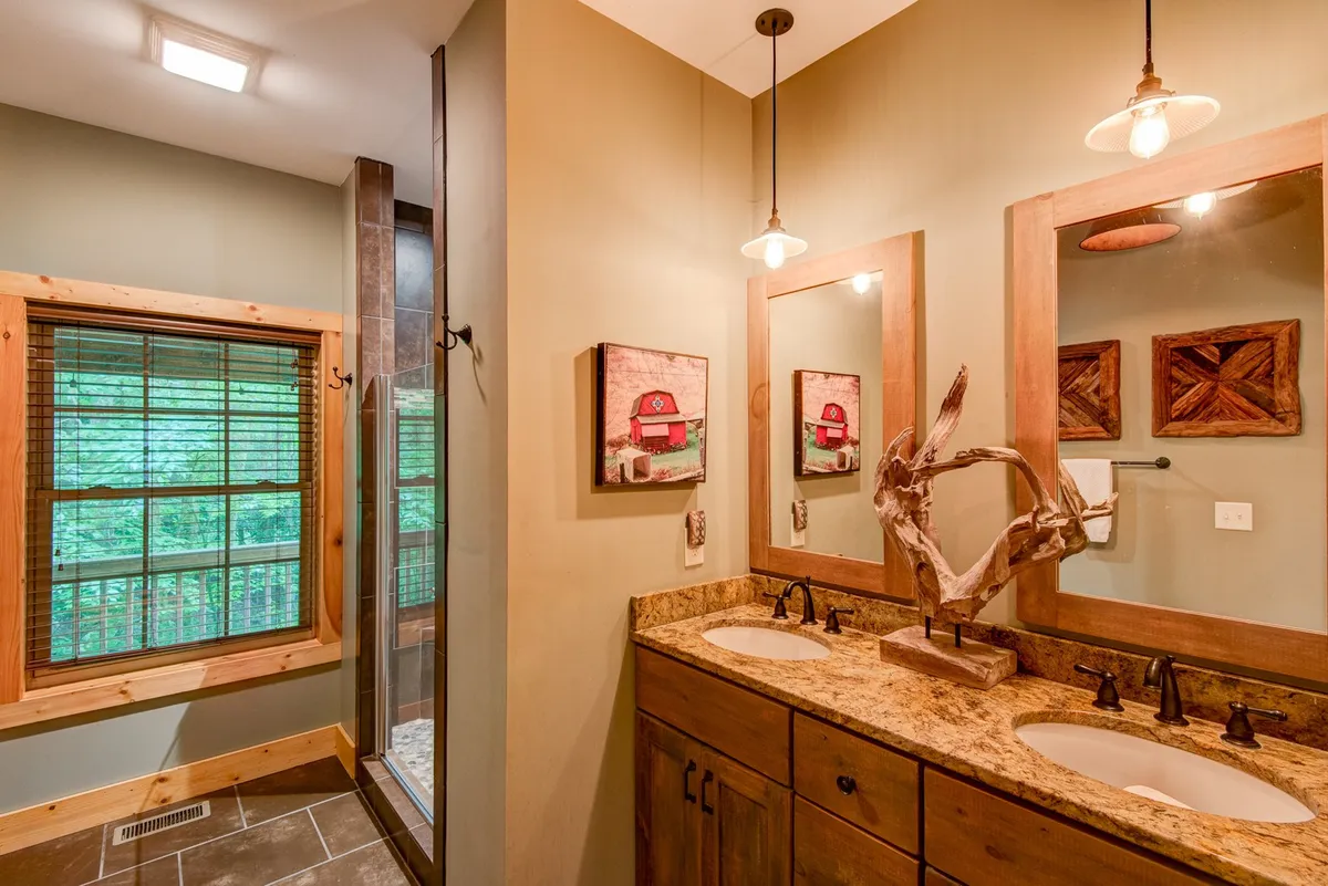 A modern bathroom featuring double sinks with wooden cabinetry, framed mirrors, and tasteful wall art. The space feels bright and calming, designed for both relaxation and convenient routines.
