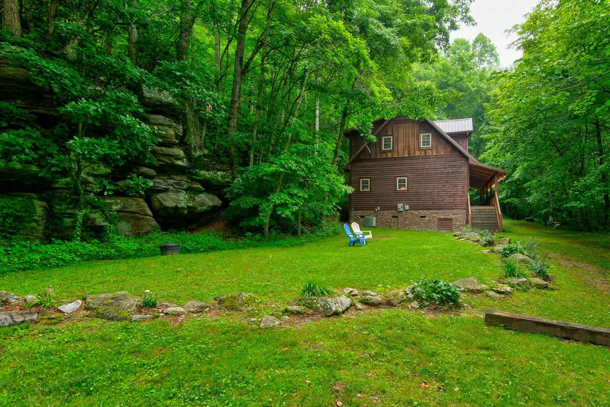 An inviting view of the wooden cabin with a green lawn, lounge chairs, and natural rock features, all set against a scenic outdoor backdrop. This space encourages both people and pets to unwind, play, and soak in the mountain setting.